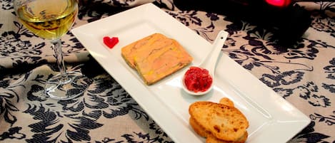A plate with a slice of cake, a spoon with jam, and a glass of white wine on a tablecloth.
