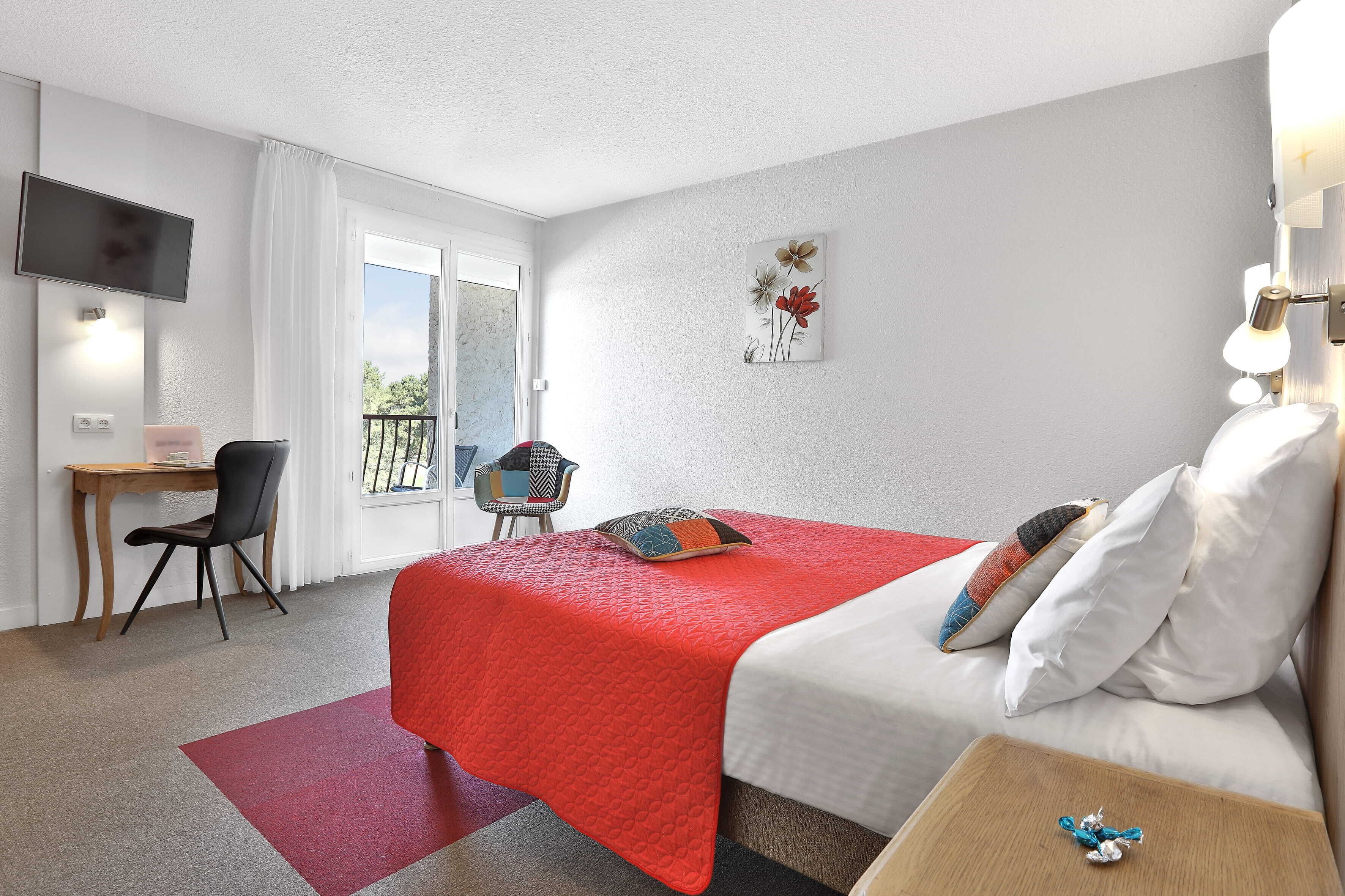 Ein Hotelzimmer mit Bett, Schreibtisch, Stuhl, Fernseher und einem Balkon.