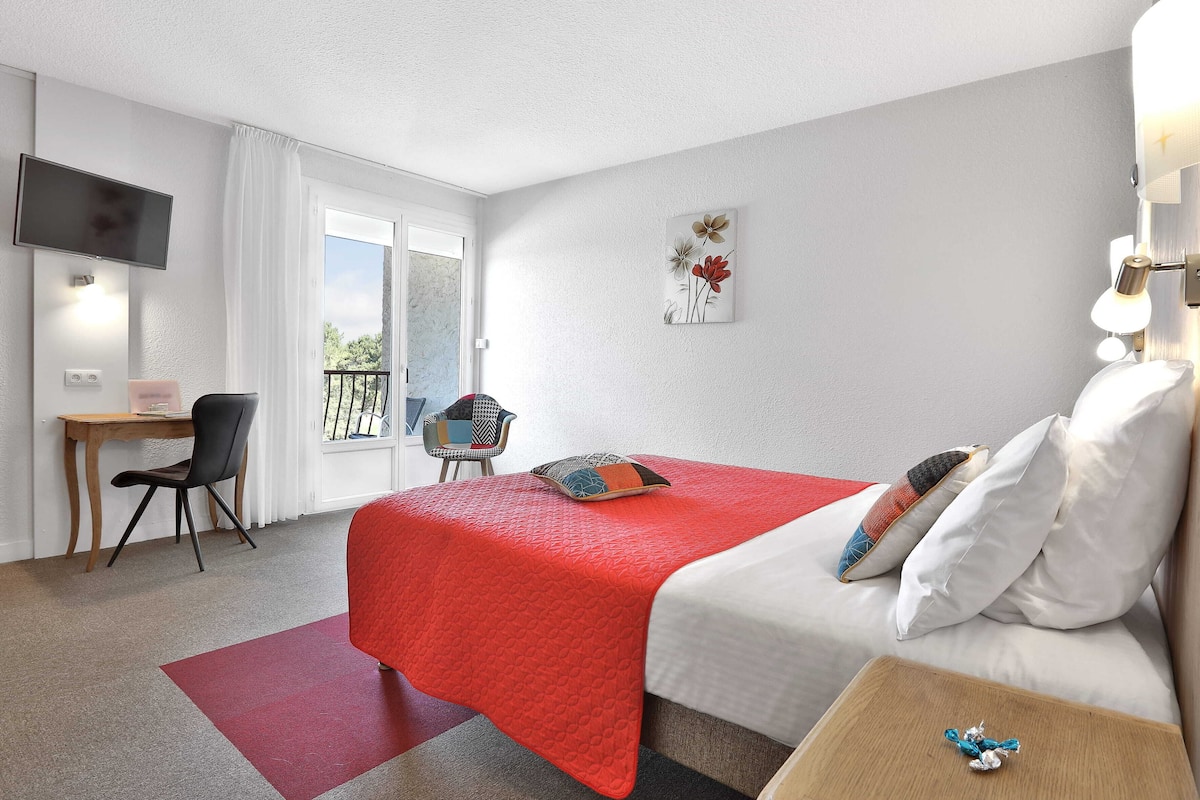 Una habitación de hotel con cama, escritorio, silla, televisión y balcón.