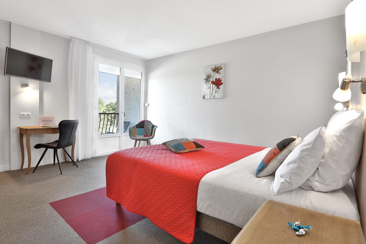 Een hotelkamer met een bed, een bureau, een stoel, een televisie en een balkon.