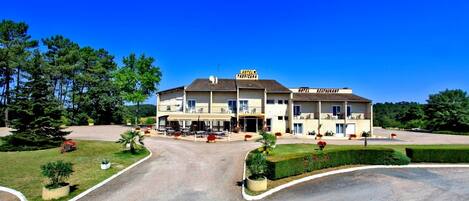 Un hotel con bar y restaurante centrales, varios balcones y un césped bien cuidado.