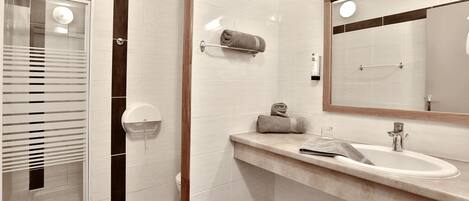 Un baño moderno con cabina de ducha de vidrio, un lavabo con toallero y un espejo.