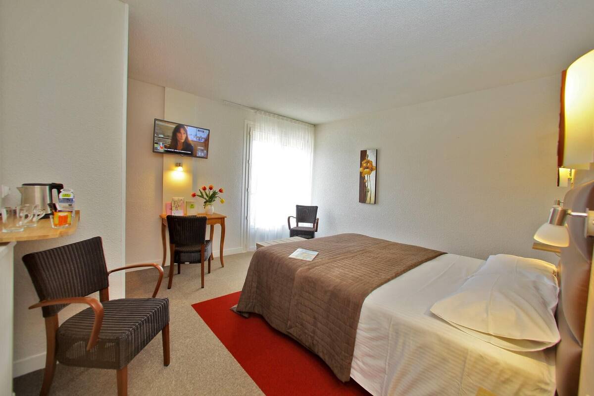 Una habitación de hotel con cama, escritorio, silla, televisor y un cuadro en la pared.