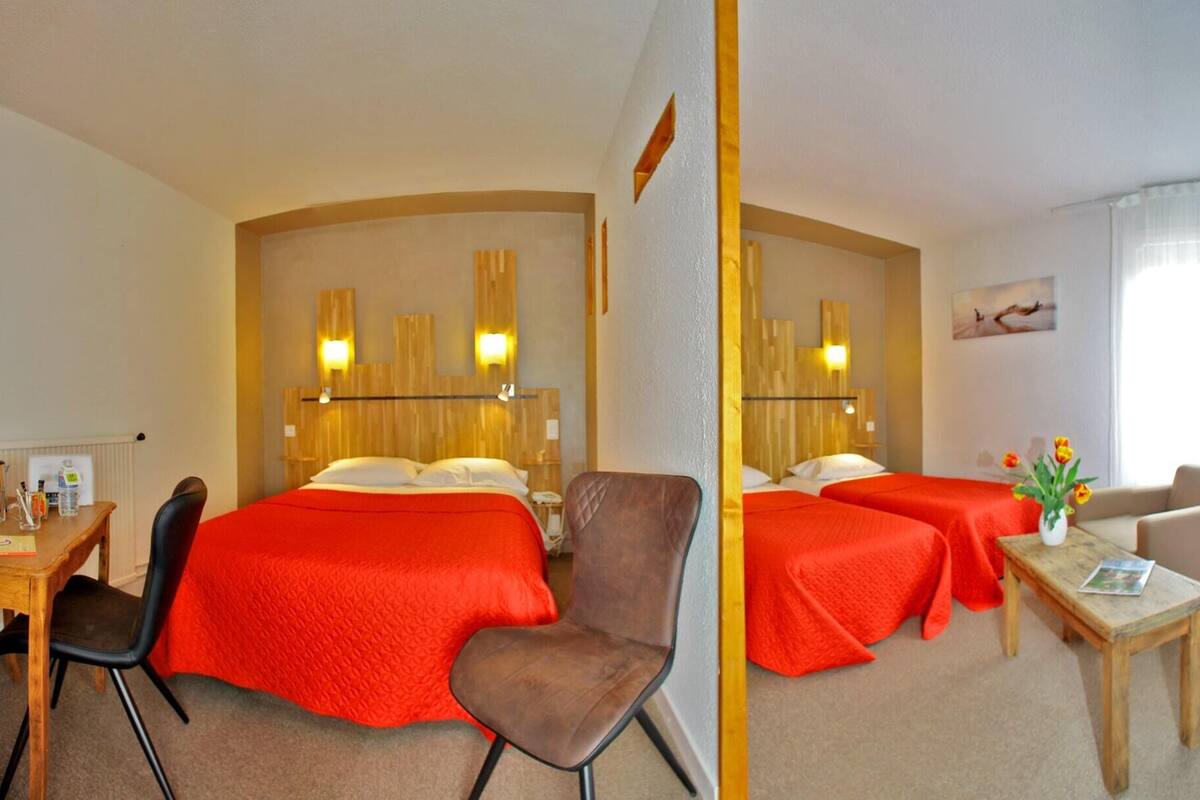 Habitación de hotel con dos camas, un escritorio, una silla y una mesita con un florero.