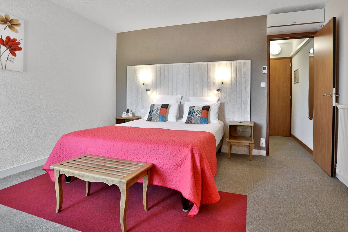 Een hotelkamer met een bed, nachtkastjes, een bankje en een deur.