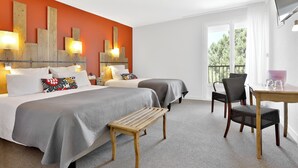 Een hotelkamer met twee bedden, een houten bankje, een tafel met stoelen en een groot raam met uitzicht op bomen.