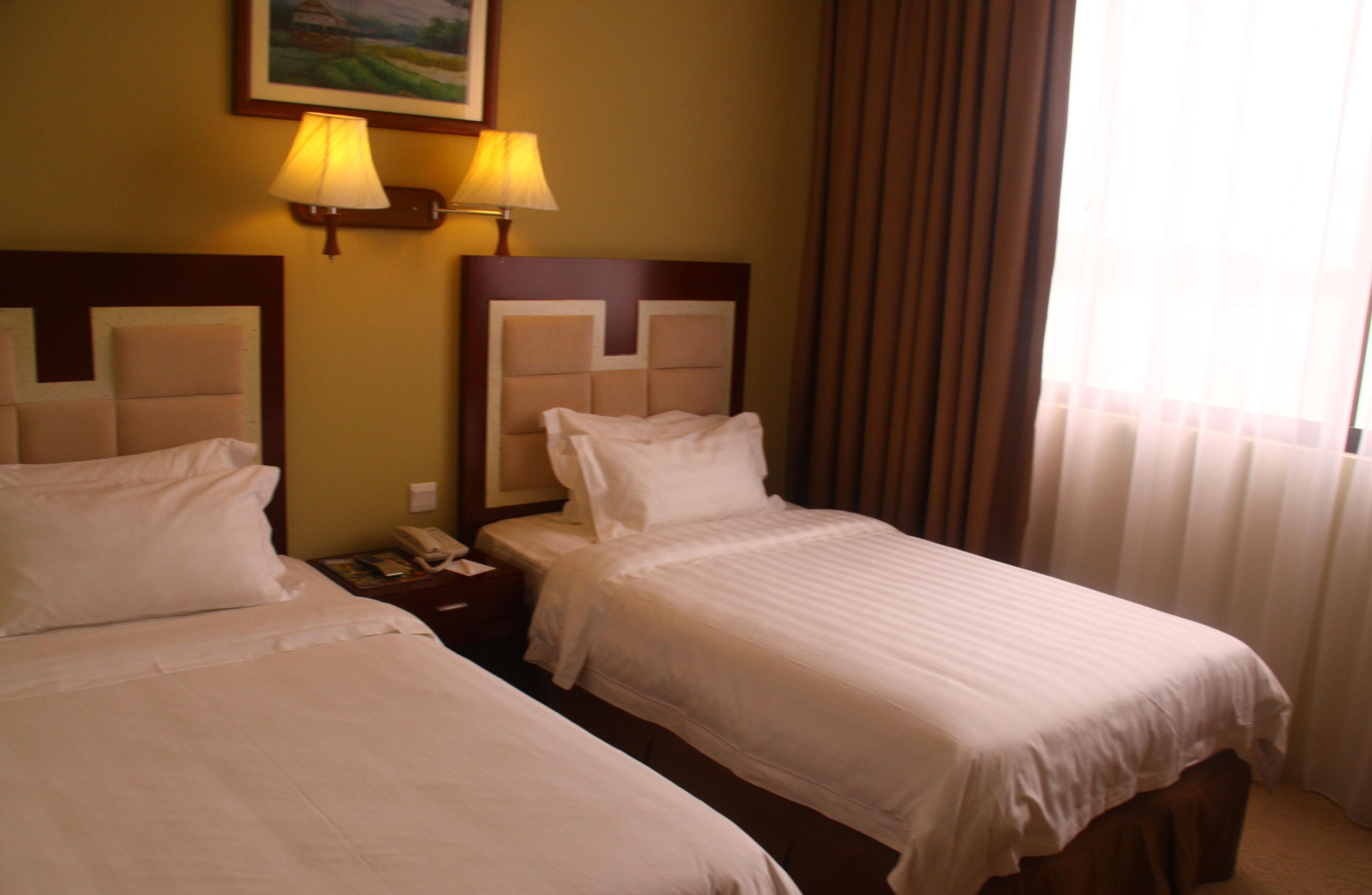 A hotel room with two beds, a nightstand with a phone, and two wall-mounted lamps.