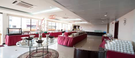 A spacious room with a buffet setup, large windows, and a modern ceiling design.