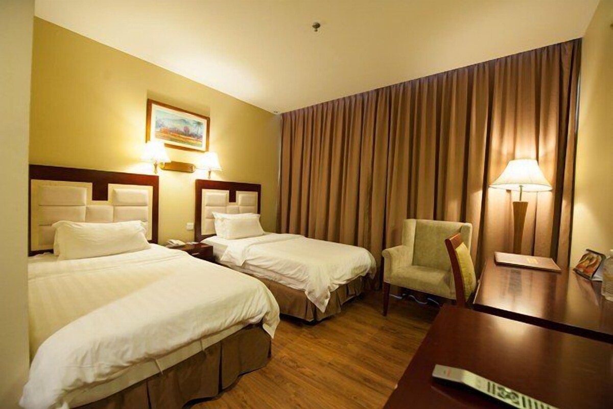 Ett hotellrum med två sängar, en stol, ett bord och en tavla på väggen.