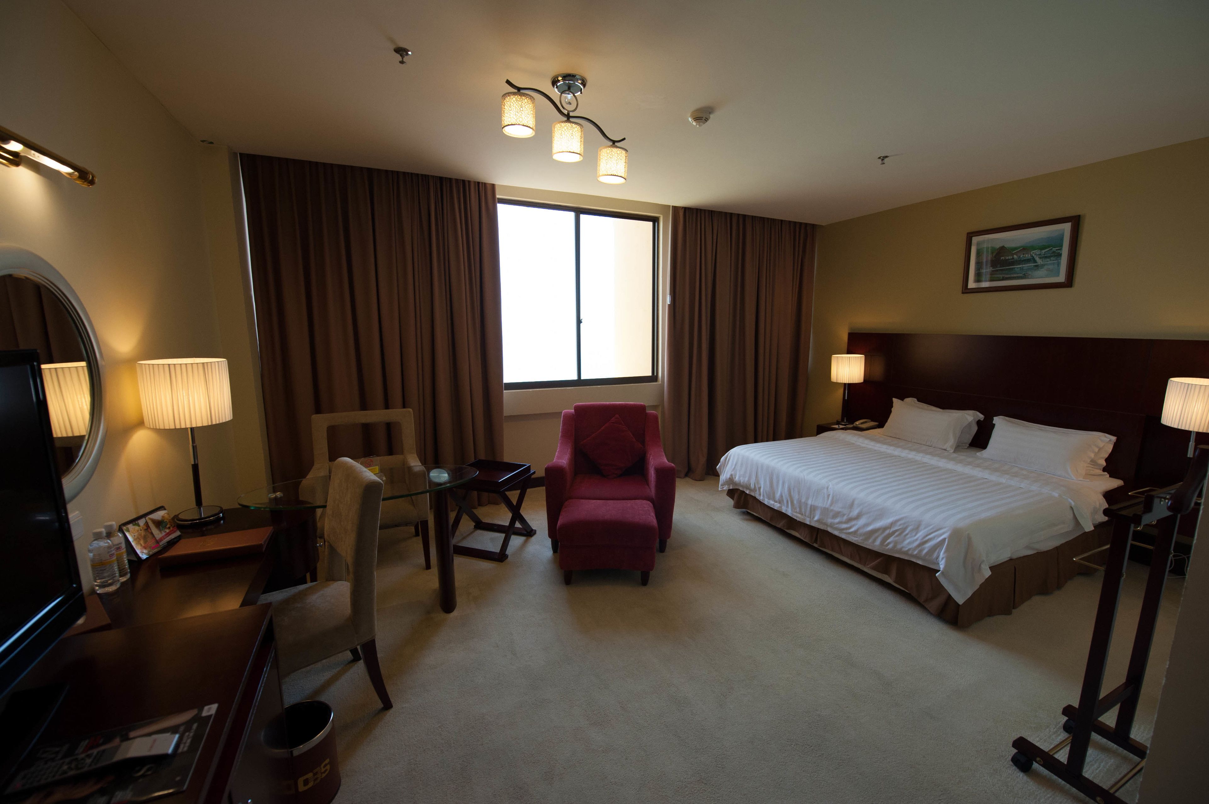 A hotel room with a bed, a desk, a chair, a television, and a large window.