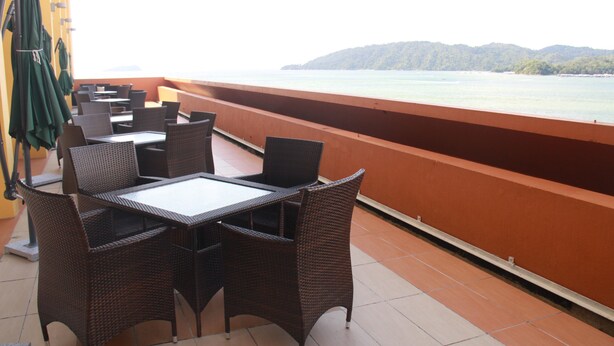 A terrace with wicker furniture, a table, and chairs, overlooking a body of water and hills. - Gaya Centre Hotel (Kota Kinabalu)