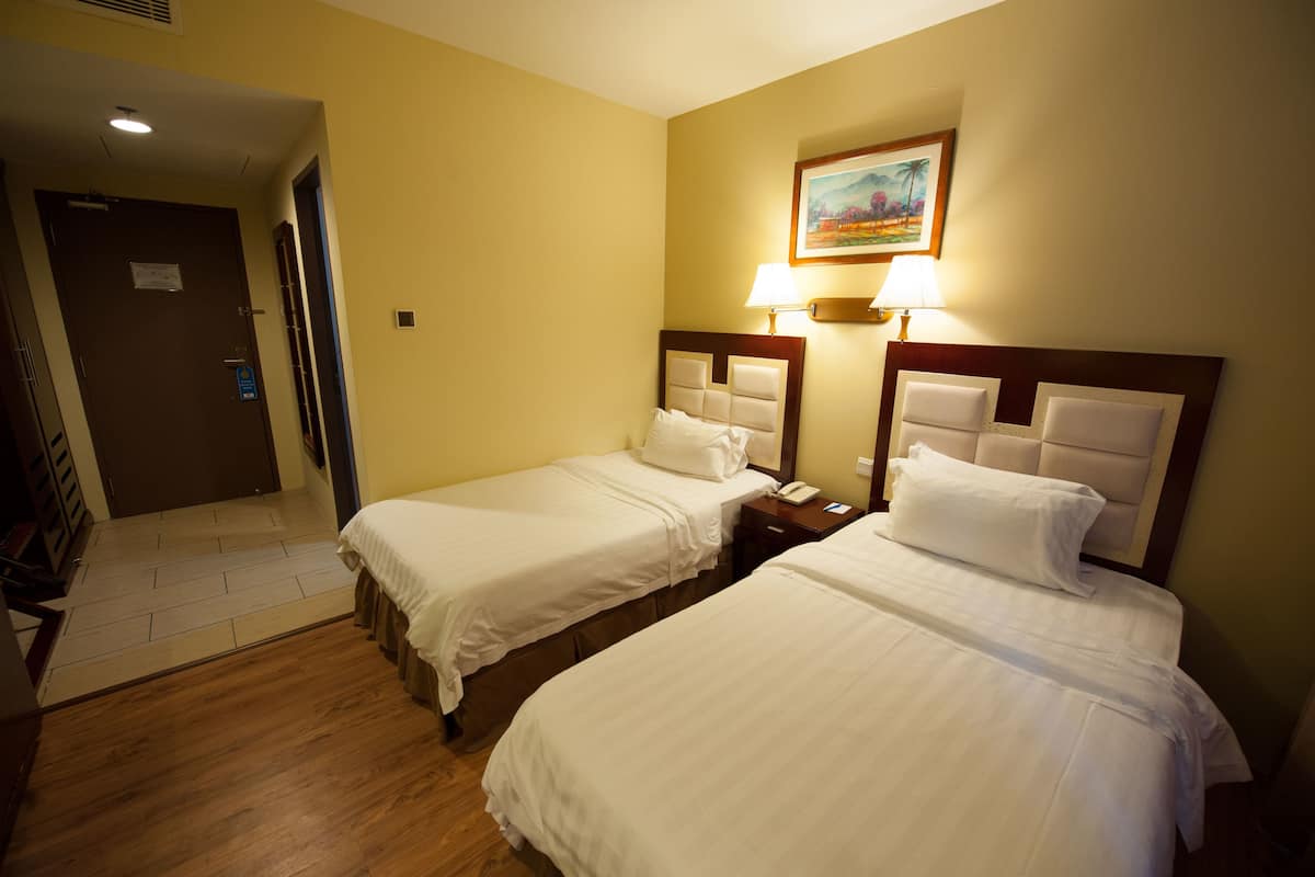 Habitació d'hotel amb dos llits individuals, un sòl de fusta, un quadre a la paret i una porta que dóna a una escala.