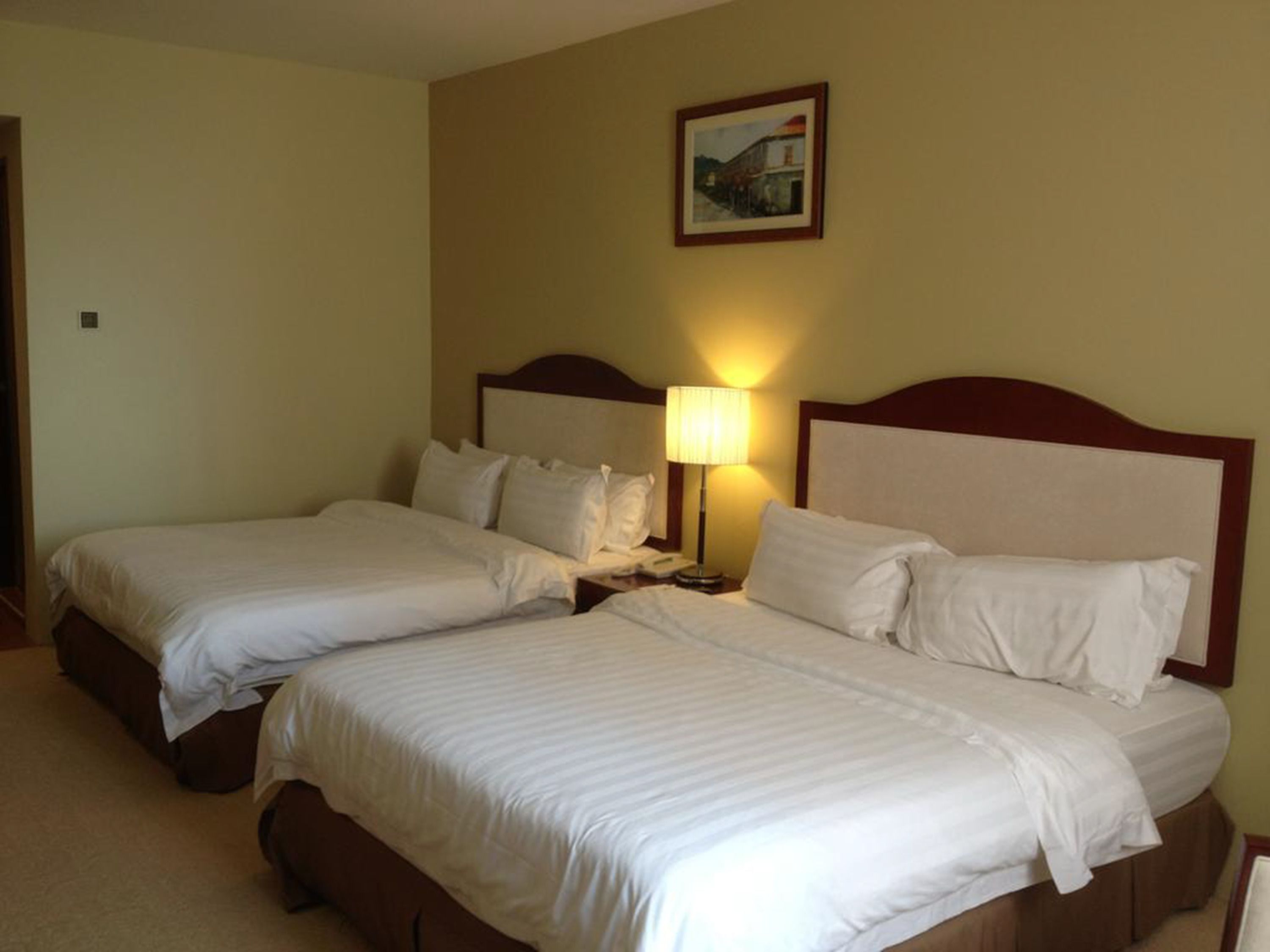 A hotel room with two single beds, a nightstand with a lamp, and a framed picture on the wall.