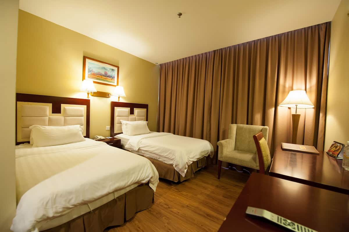 Habitació d'hotel amb dos llits, una cadira, un escriptori i una làmpada.