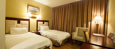Una habitación de hotel con dos camas, una silla, un escritorio y una lámpara.