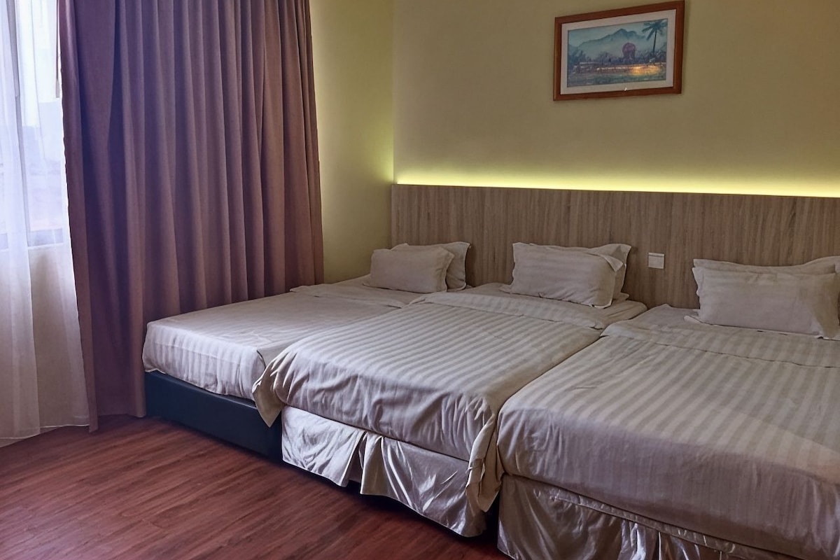 Ett hotellrum med två sängar, ett trägolv, en tavla på väggen och ett fönster med gardiner.