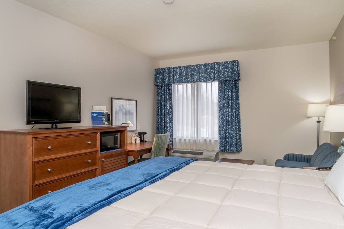 Una habitación de hotel con una cama, un escritorio con computadora, televisor y ventana con cortinas.