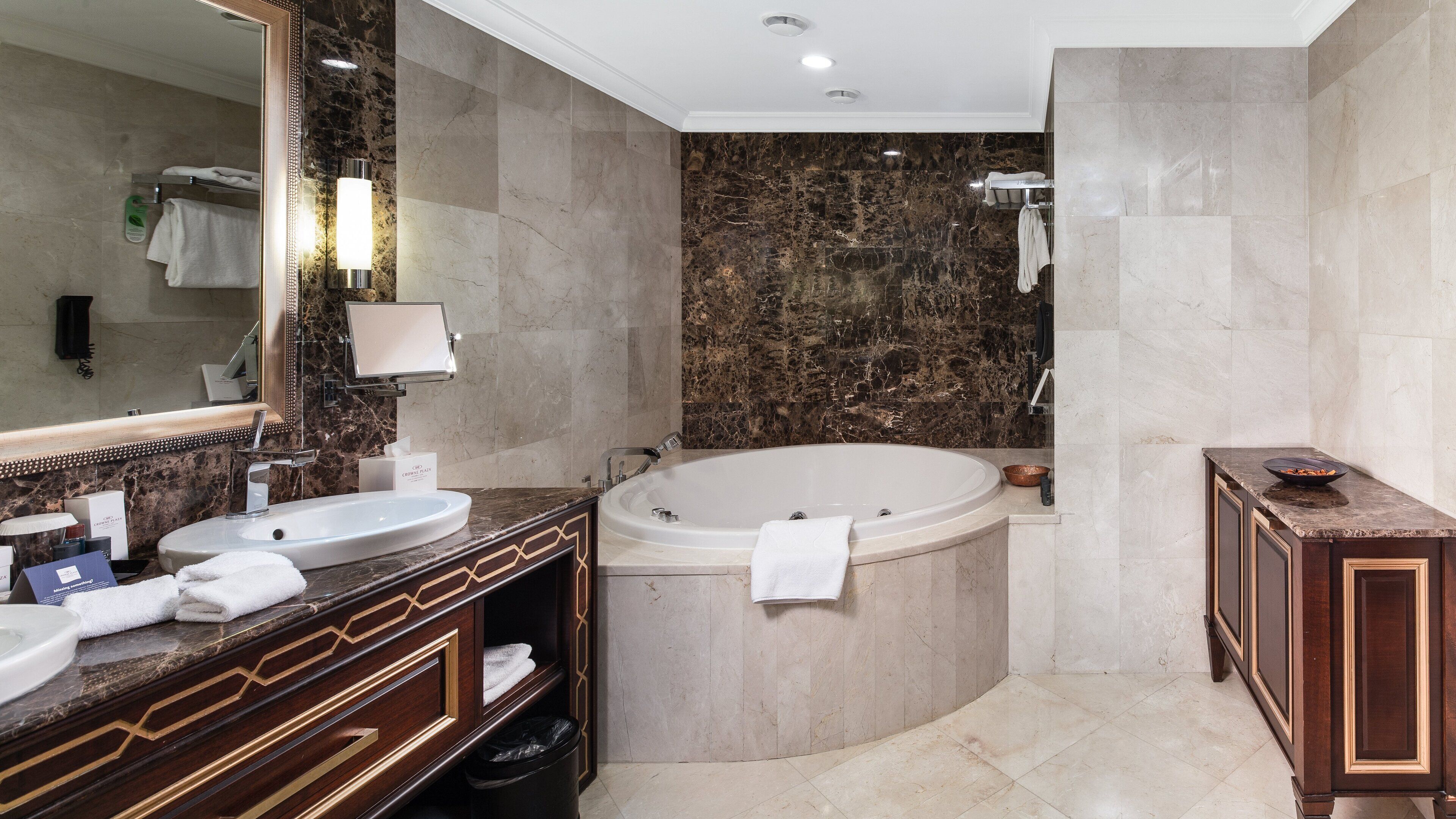 A bathroom with a large bathtub, two sinks, a vanity with a mirror, and a towel rack.