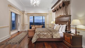 A spacious bedroom with a large bed, a nightstand, a chair, and a view of the city.