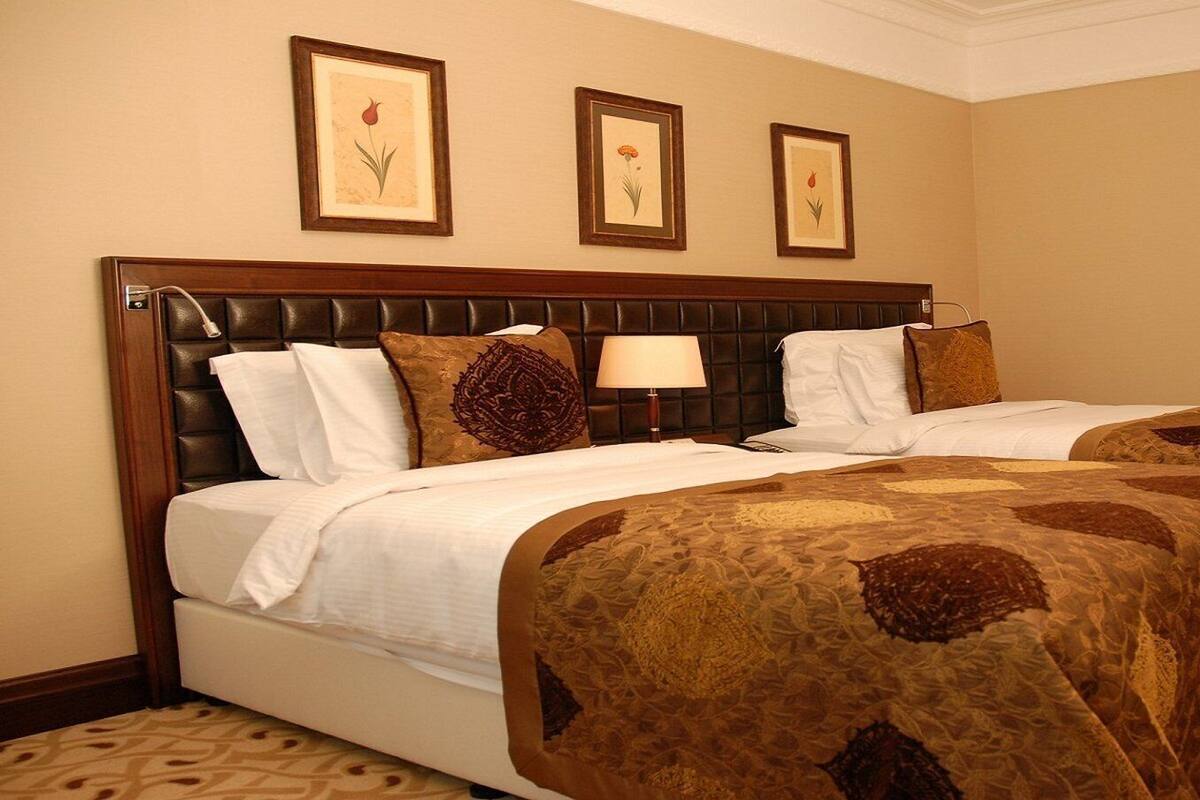 A hotel room with two beds, a headboard, a lamp, and three framed botanical prints on the wall.