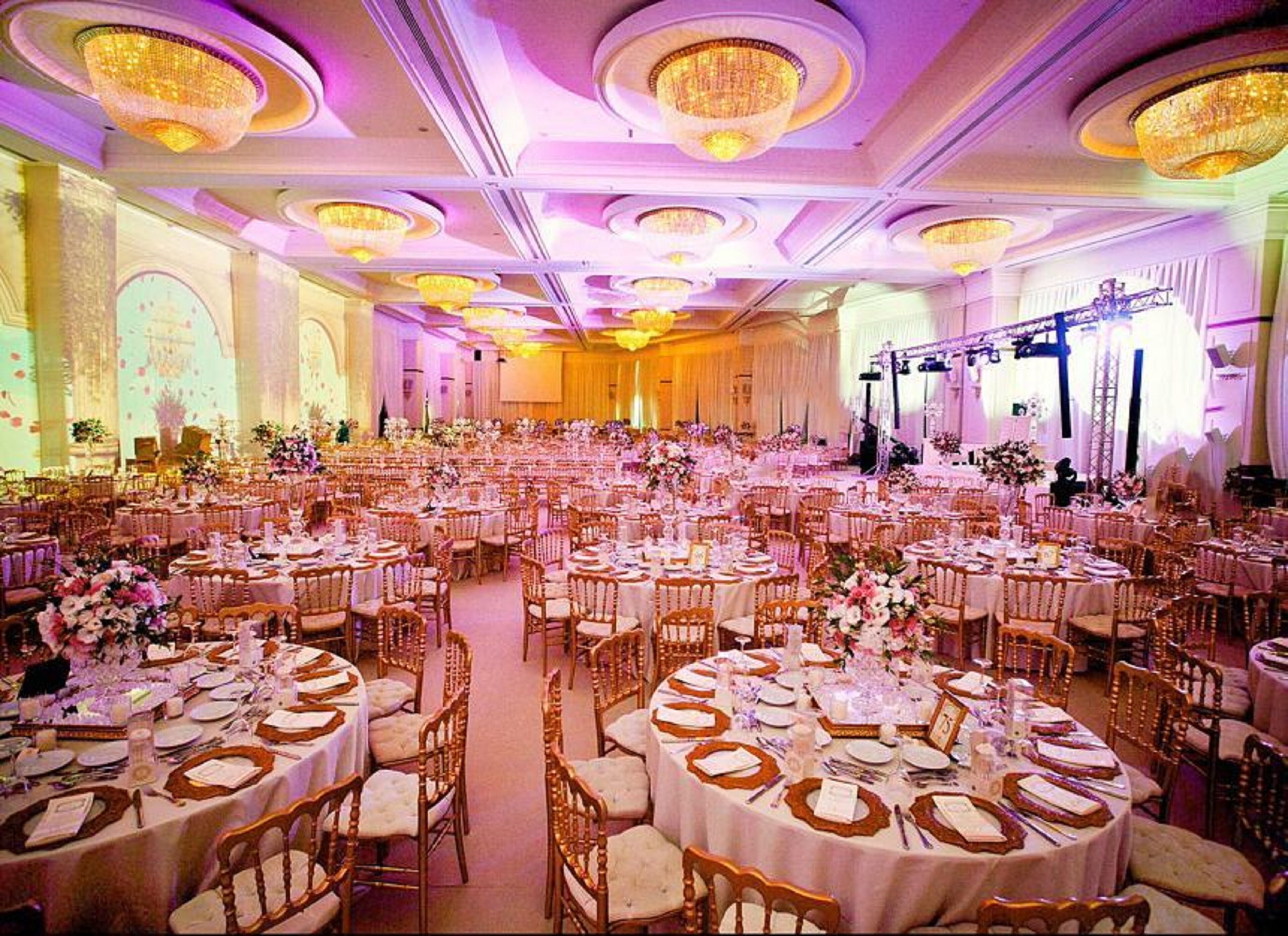 A large banquet hall with round tables set for dining, featuring chandeliers and floral centerpieces.