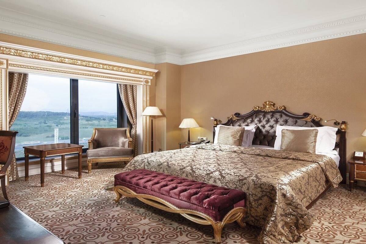 A hotel room with a large bed, a desk, a chair, and a view of the outdoors.