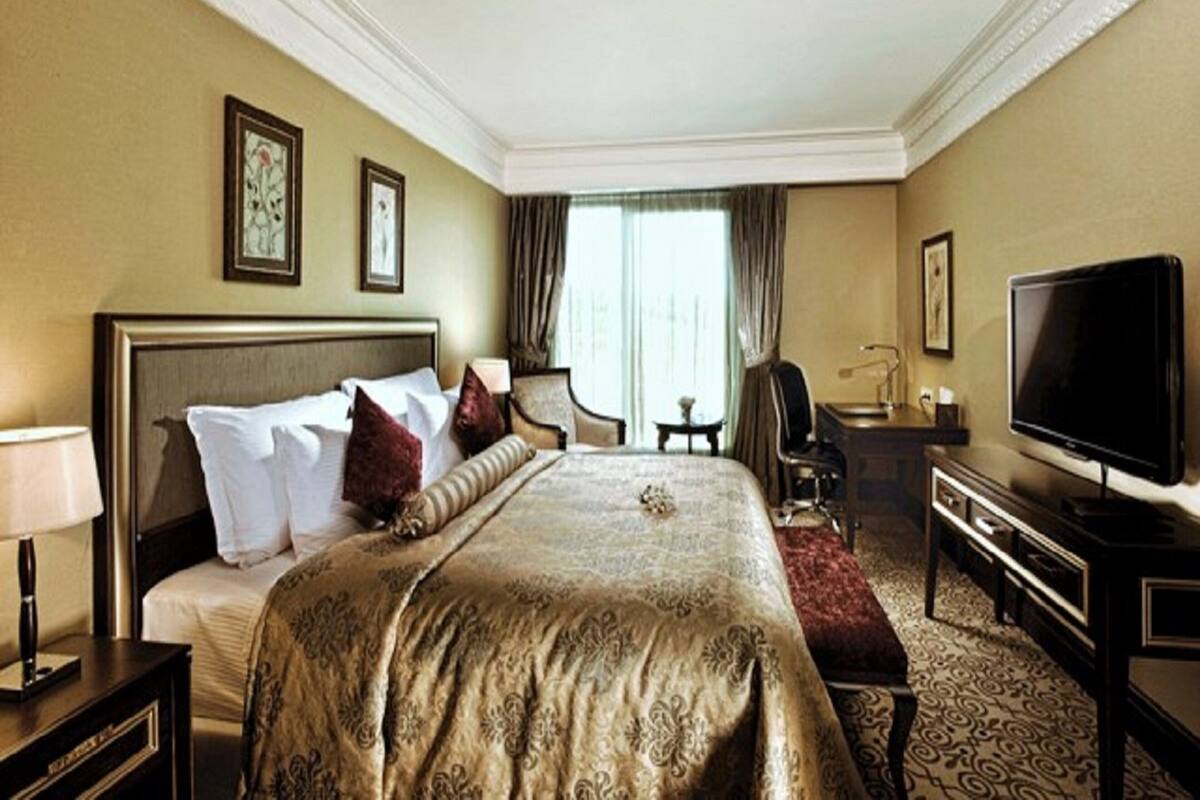 A hotel room with a large bed, a desk, a chair, a television, and a window with curtains.
