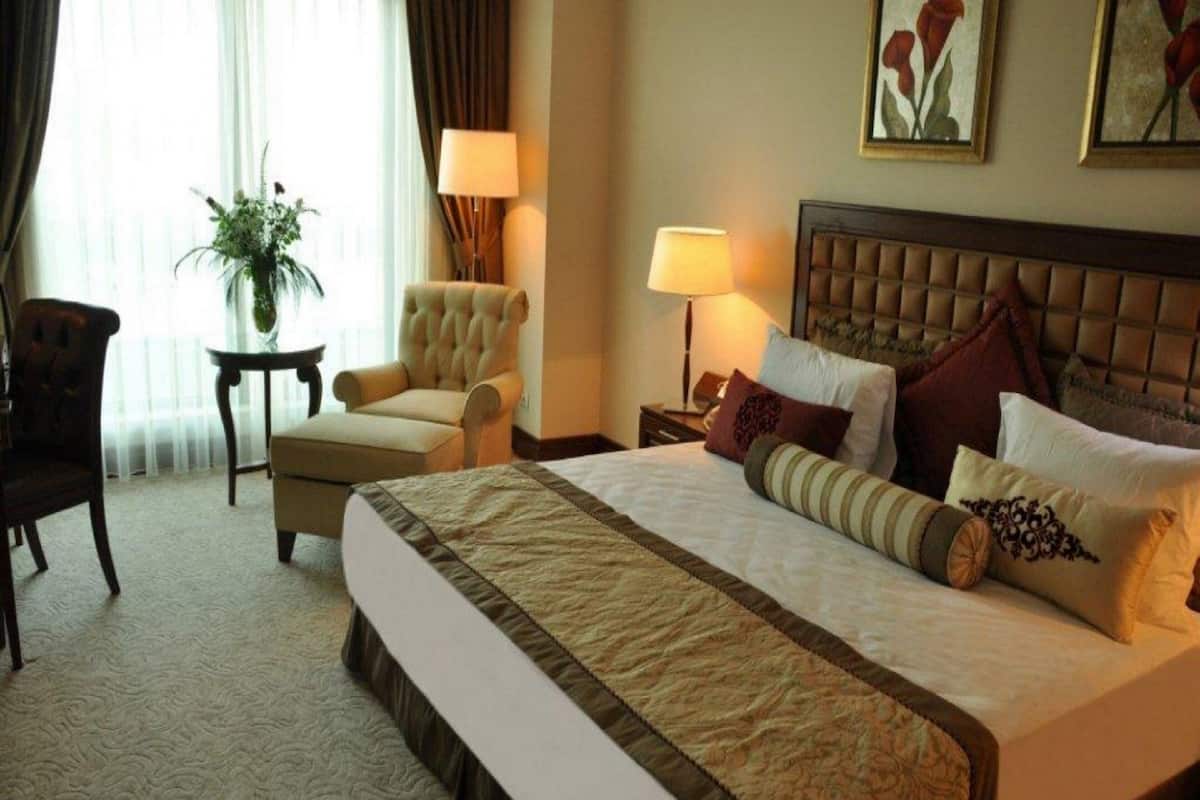 A hotel room with a large bed, a chair, a small table, and a lamp.
