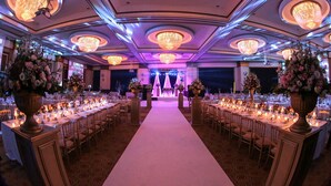 A banquet hall with a central aisle, round tables, and chandeliers.