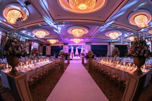 Een balzaal met een middenpad, ronde tafels en kroonluchters.