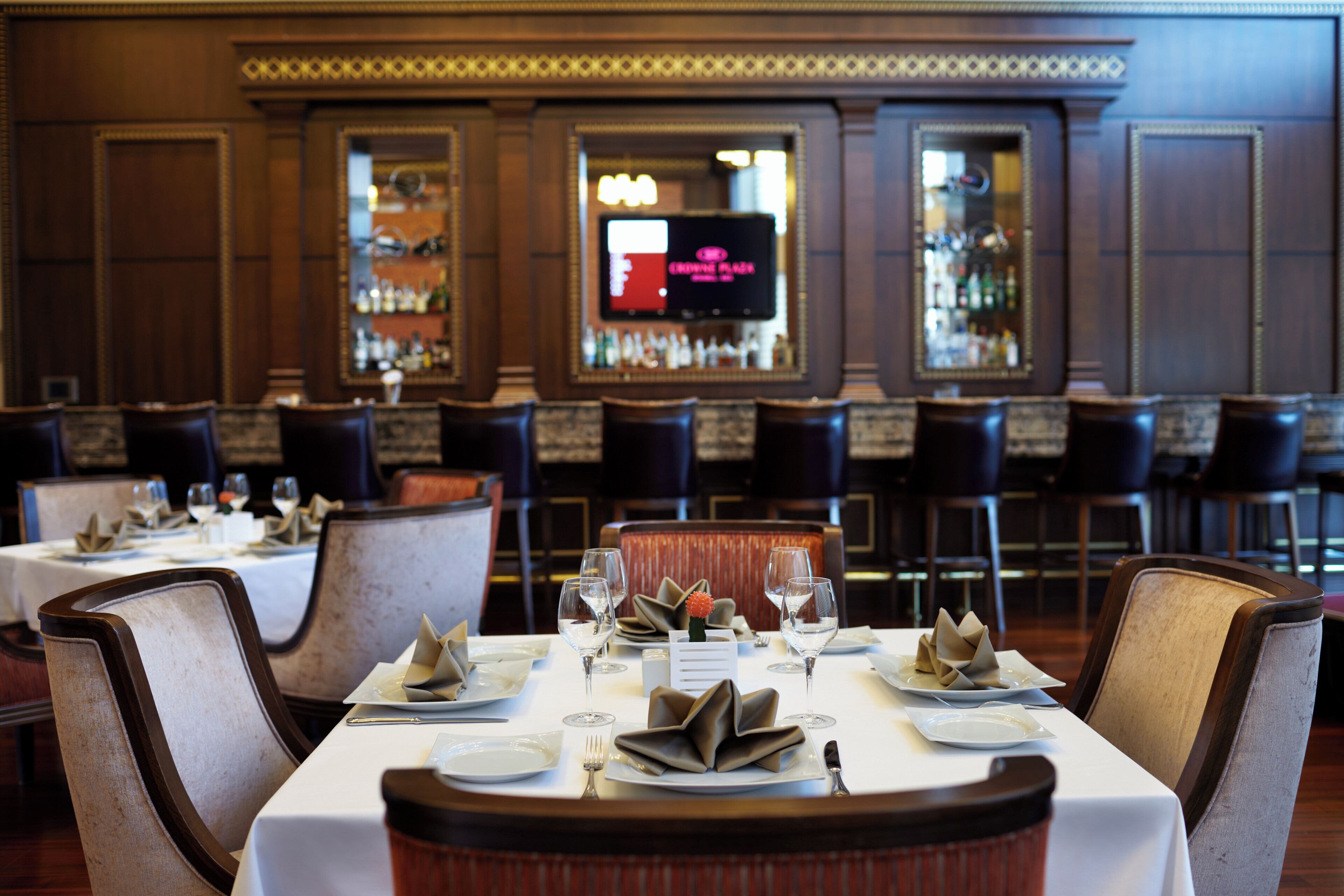 A restaurant interior with tables set for dining, chairs, and a bar area with bottles.