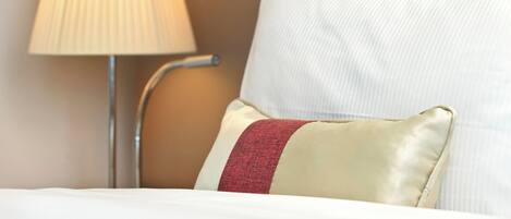 A neatly made bed with white bedding and a single red accent pillow.