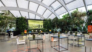A spacious indoor area with tables and chairs, a large screen, and greenery.