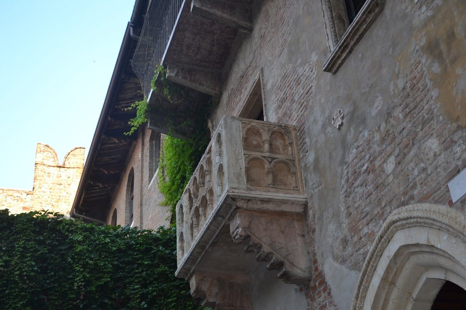 Un bâtiment historique doté d’une façade en pierre, de fenêtres en arc de cercle et d’un balcon orné de plantes grimpantes.
