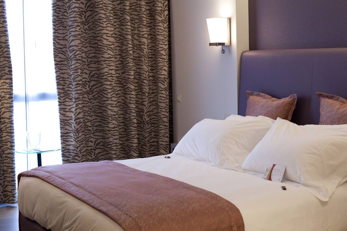 Een hotelkamer met een groot bed, een glazen tafel en kamergordijnen met een patroon.