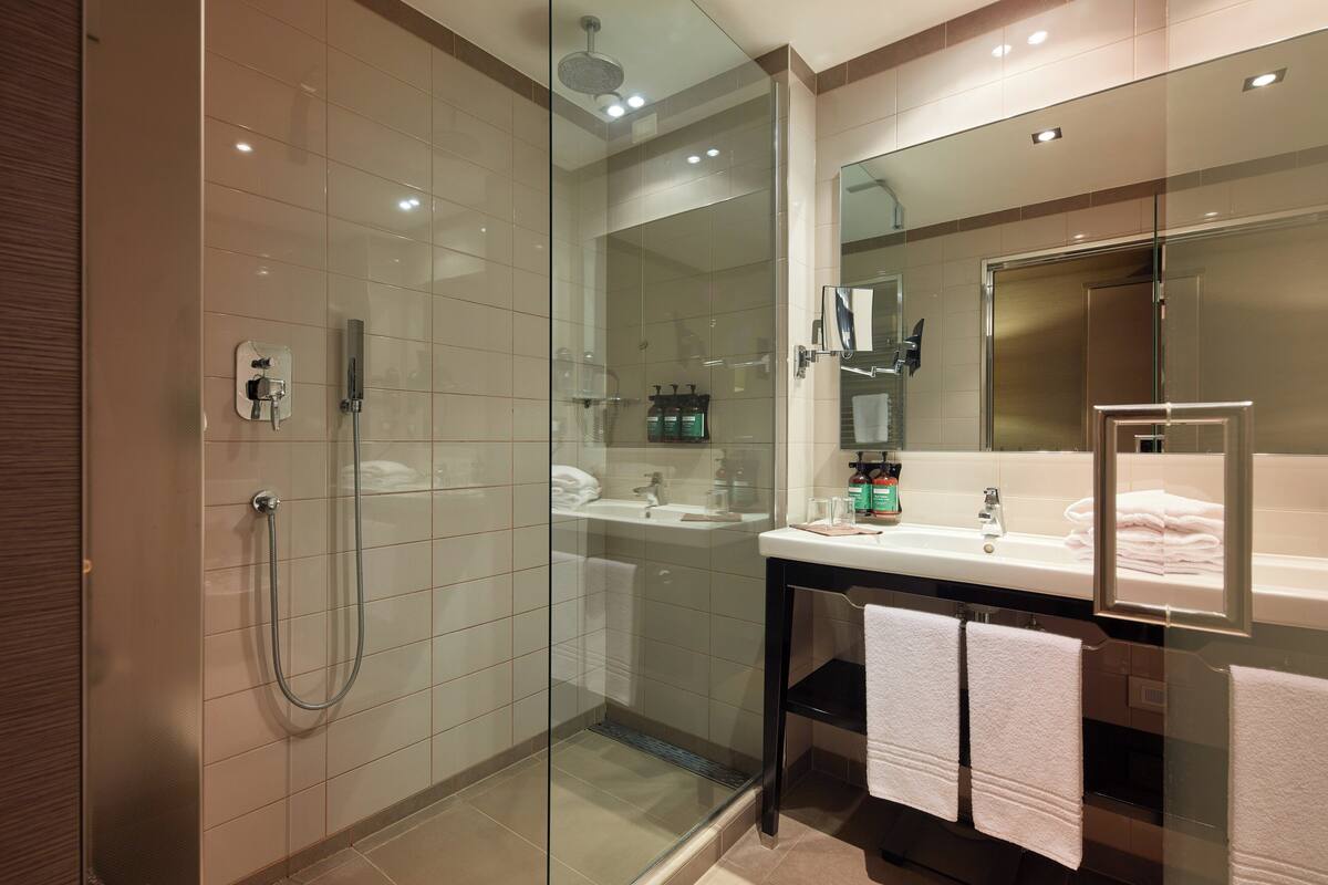 Een moderne badkamer met een douche met glazen wand, een wastafel met spiegel, en twee handdoeken aan de muur.