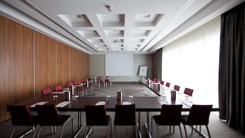 Una sala de conferencias con una mesa larga, sillas rojas, una pizarra y una pantalla de proyector.