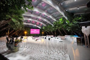 Un espacio para eventos en interiores con escenario, asientos y una gran pantalla que muestra 'CROWNE PLAZA VERONA'.