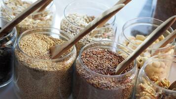 Varios frascos de vidrio llenos de diferentes cereales y frutos secos, cada uno con una cuchara de madera.