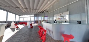 Un espace bar moderne avec un comptoir, des tabourets rouges et une vitrine où sont exposées les bouteilles.