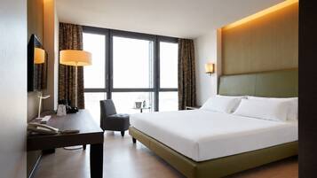 Une chambre d’hôtel avec un grand lit, un bureau avec un téléphone, une chaise et une fenêtre avec des rideaux.