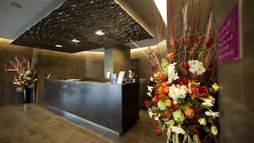 A reception desk with a modern design, a receptionist, and a large floral arrangement.