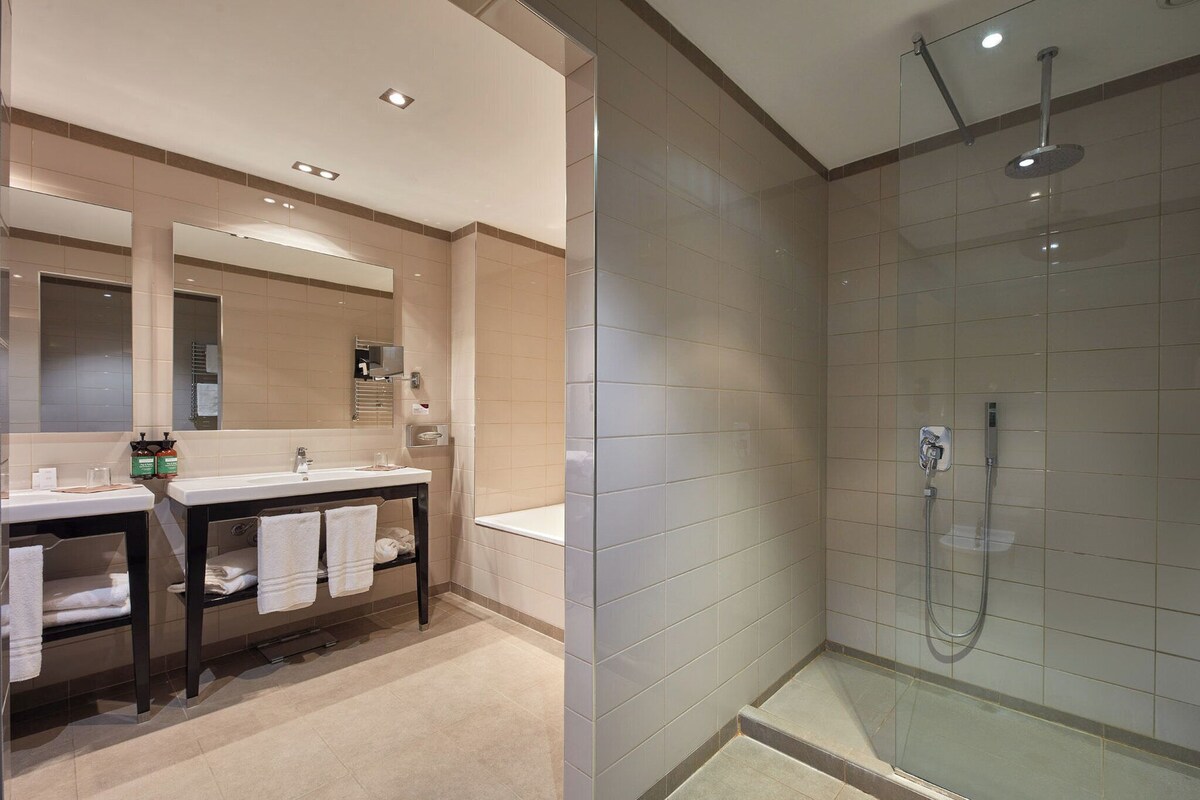 Une salle de bain moderne dot ée d’un meuble-lavabo à deux vasques, d’un grand miroir et d’une cabine de douche en verre.