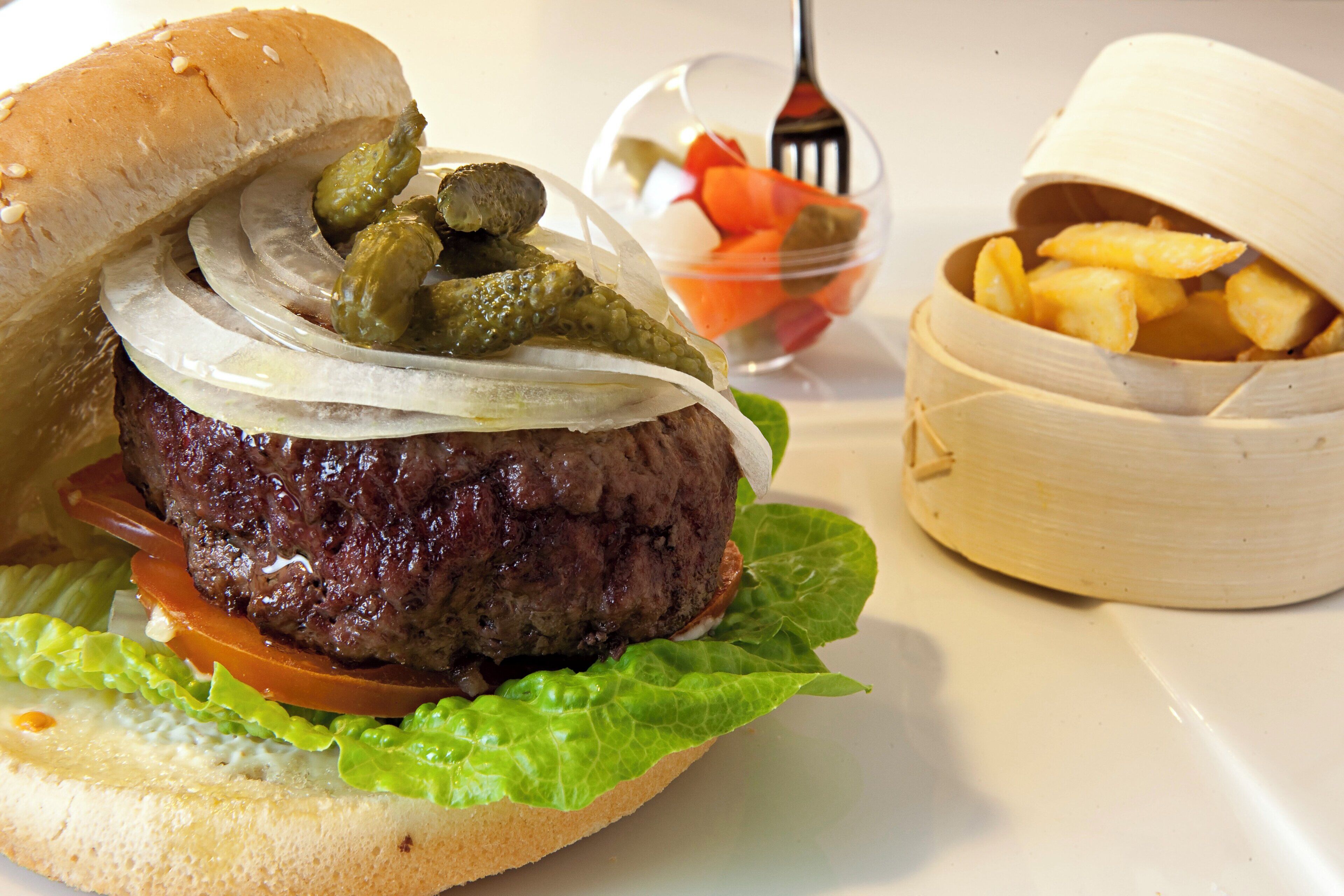 Una hamburguesa con pepinillos y cebollas, una porción de papas fritas y un recipiente pequeño de kétchup.