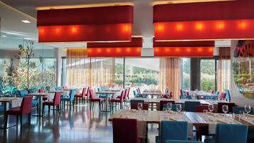 A restaurant with multiple tables and chairs, large windows, and hanging red lamps.