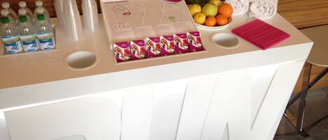 A reception desk with bottled water, a map, fruit, and towels.