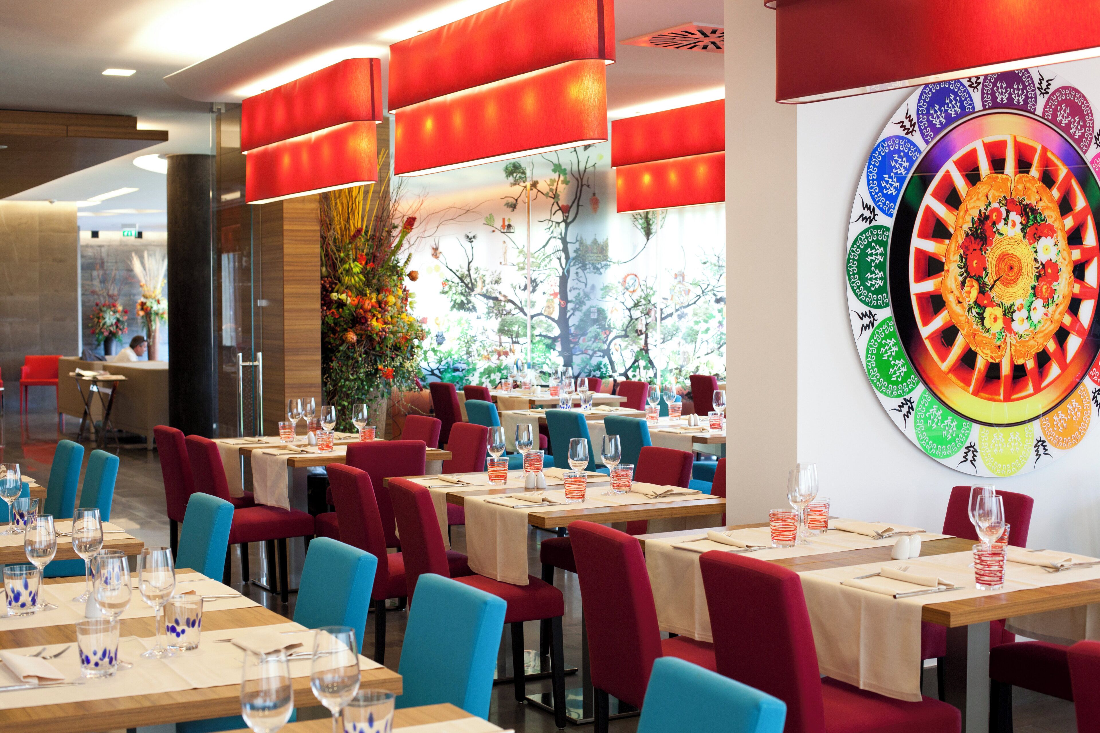 A restaurant interior with multiple tables, chairs, and a large decorative wall piece.