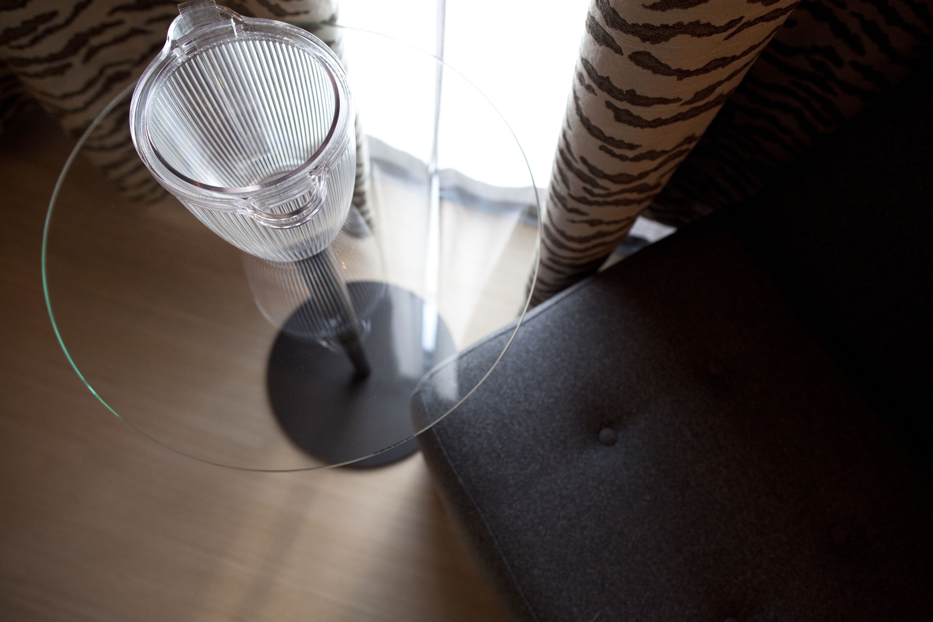 A glass table with a metal mesh object on it, a zebra-patterned cushion, and a dark-colored sofa.