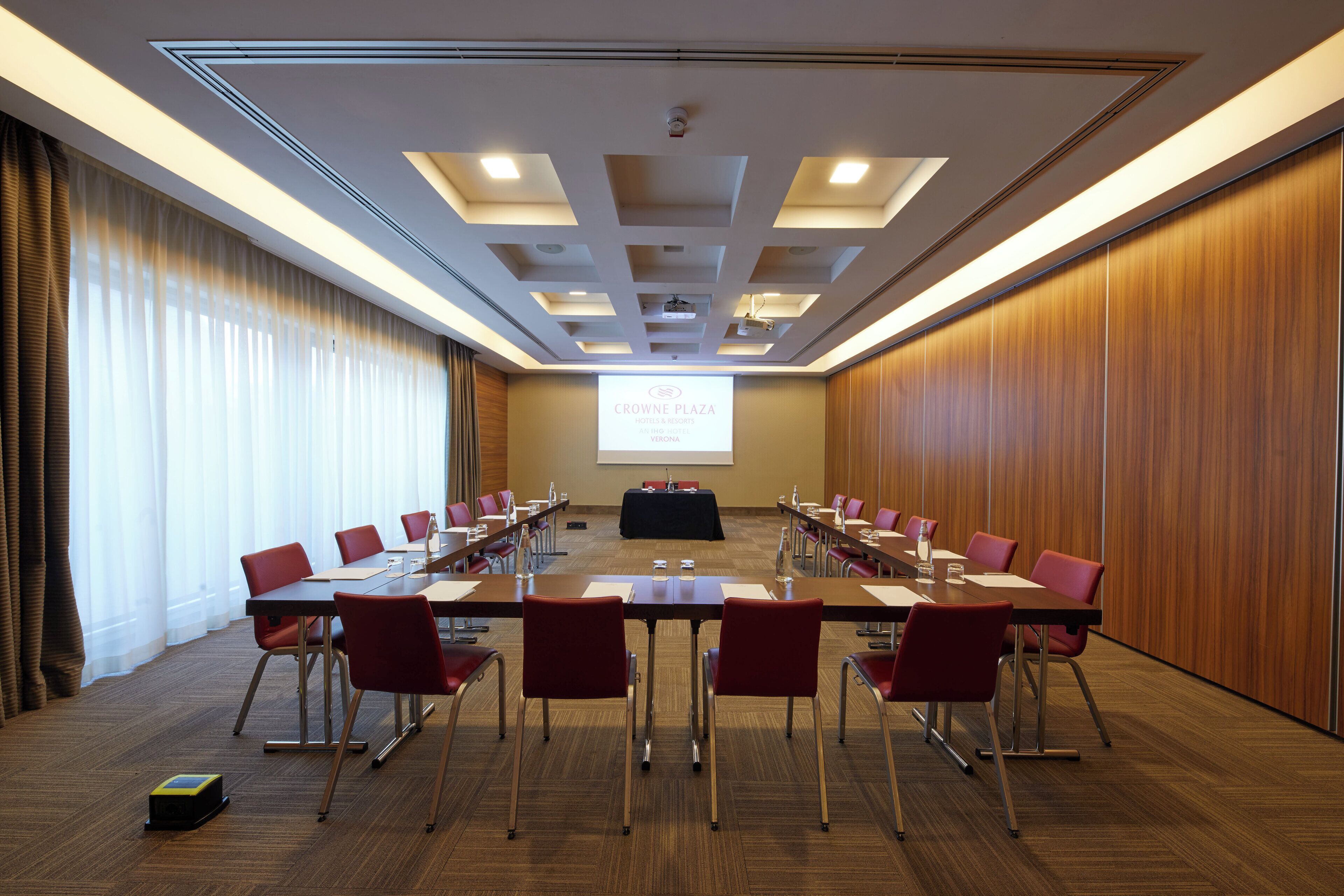 A conference room with a long table, red chairs, a projector screen, and a presentation area.