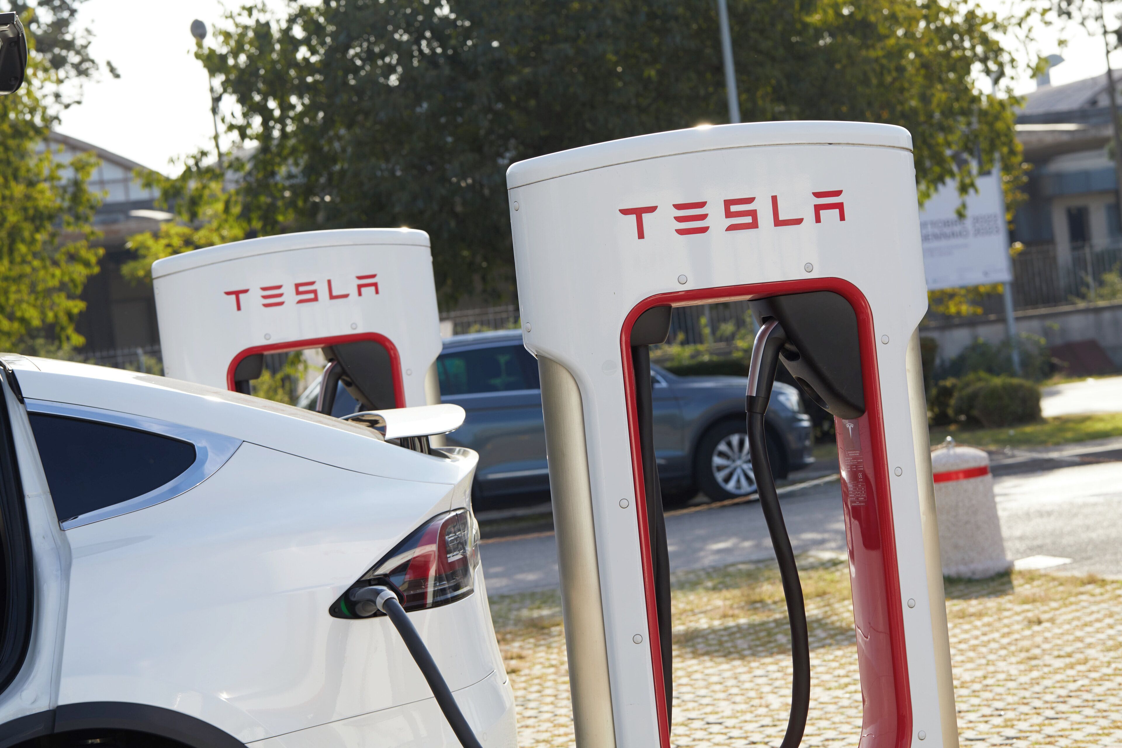 Dos estaciones de carga para vehículos eléctricos Tesla, con un coche blanco estacionado cerca.